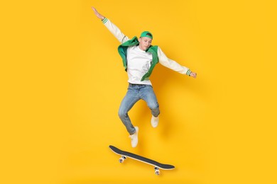 Image of Handsome man with skateboard in air on orange background. Performing trick