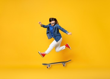 Image of Beautiful woman with skateboard in air on orange background. Performing trick