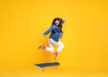 Image of Beautiful woman with skateboard in air on orange background. Performing trick