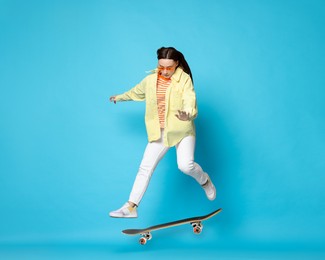 Image of Beautiful woman with skateboard in air on light blue background. Performing trick