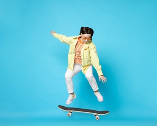 Image of Beautiful woman with skateboard in air on light blue background. Performing trick