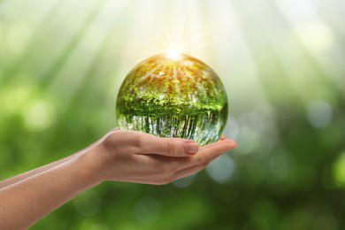 Image of Save Earth. Woman holding ball lens with overturned reflection of green forest in sunlight outdoors, closeup