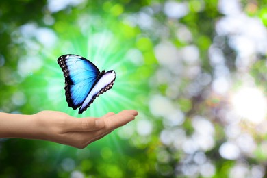 Image of Save Earth. Woman and glowing butterfly above her hand outdoors, closeup