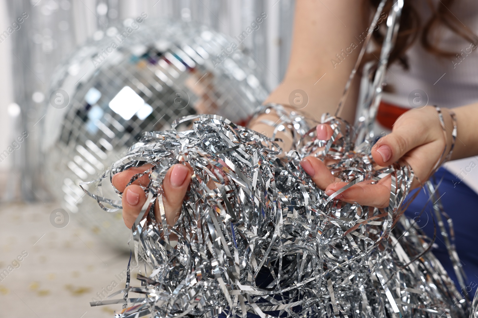 Photo of Woman with silver tinsel on floor indoors, closeup