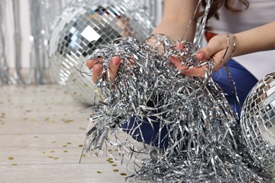 Photo of Woman with silver tinsel on floor indoors, closeup