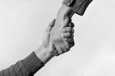 Help and support. People holding hands on light grey background, closeup. Toned in black and white