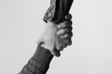 Image of Help and support. People holding hands on light grey background, closeup. Toned in black and white