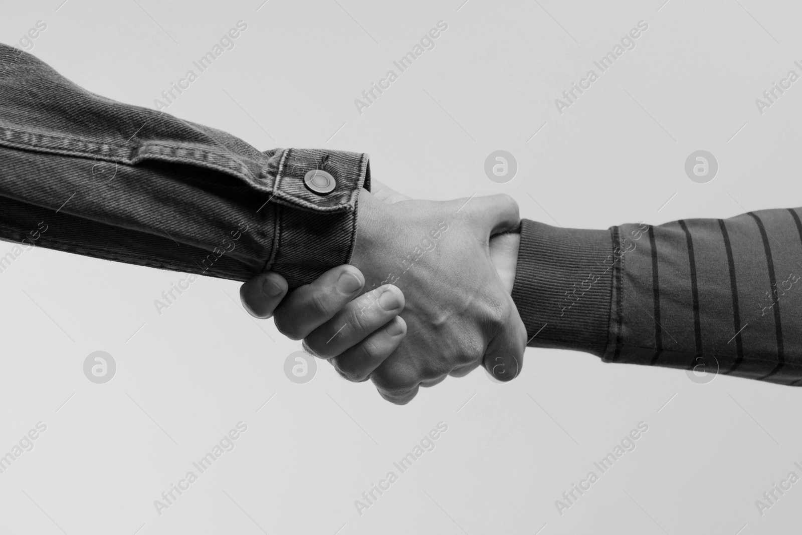 Image of Help and support. People holding hands on light grey background, closeup. Toned in black and white