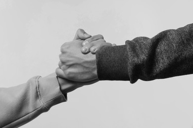 Image of Help and support. People holding hands on light grey background, closeup. Toned in black and white