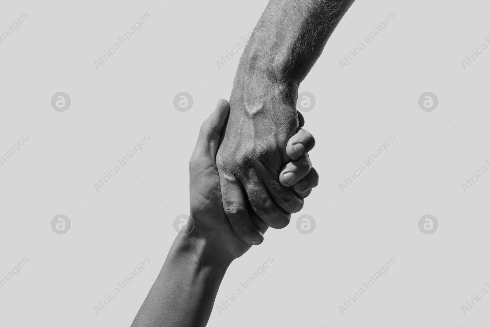 Image of Help and support. People holding hands on light grey background, closeup. Toned in black and white