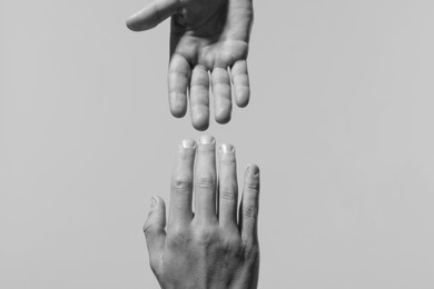 Image of Man giving helping hand to friend on light grey background, closeup. Toned in black and white