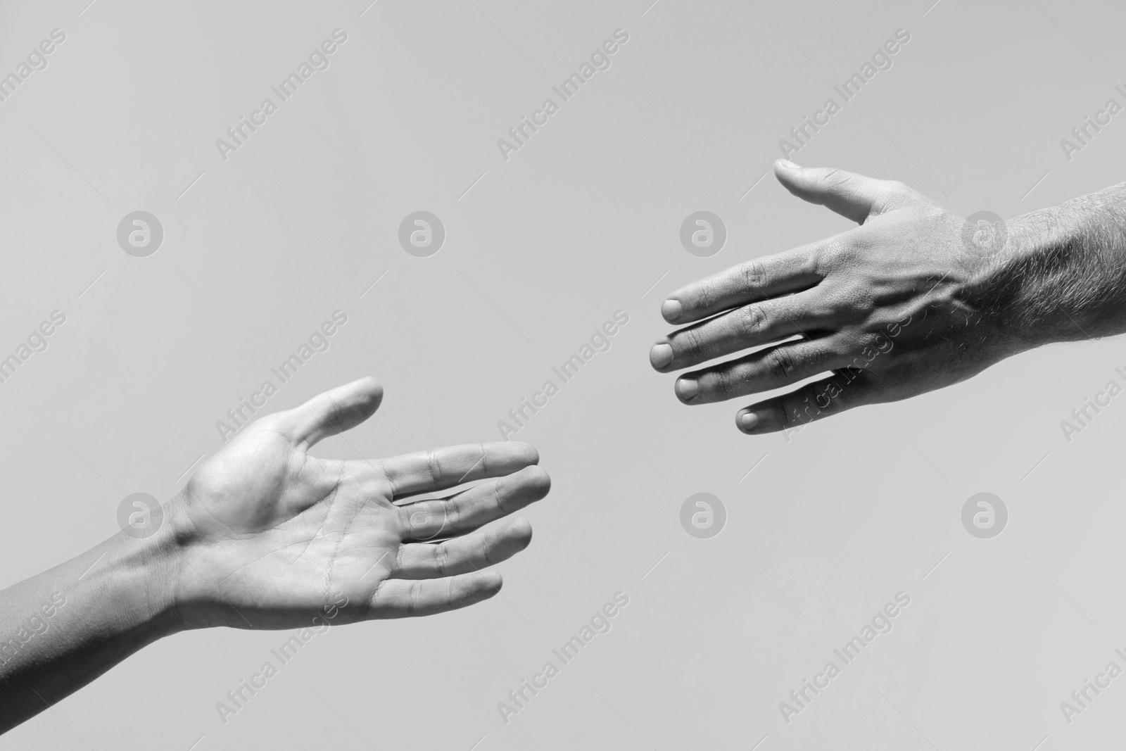 Image of Man giving helping hand to friend on light grey background, closeup. Toned in black and white