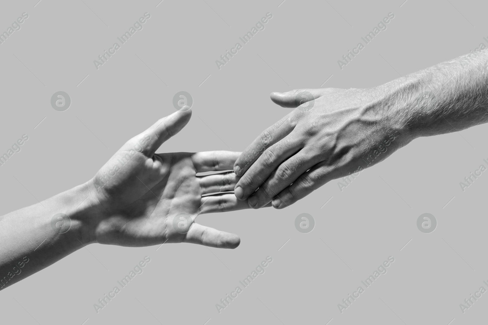 Image of Man giving helping hand to friend on light grey background, closeup. Toned in black and white