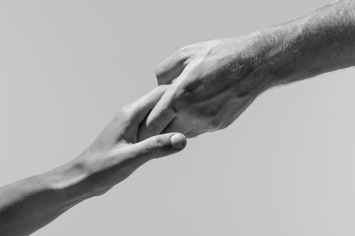 Image of Help and support. People holding hands on light grey background, closeup. Toned in black and white