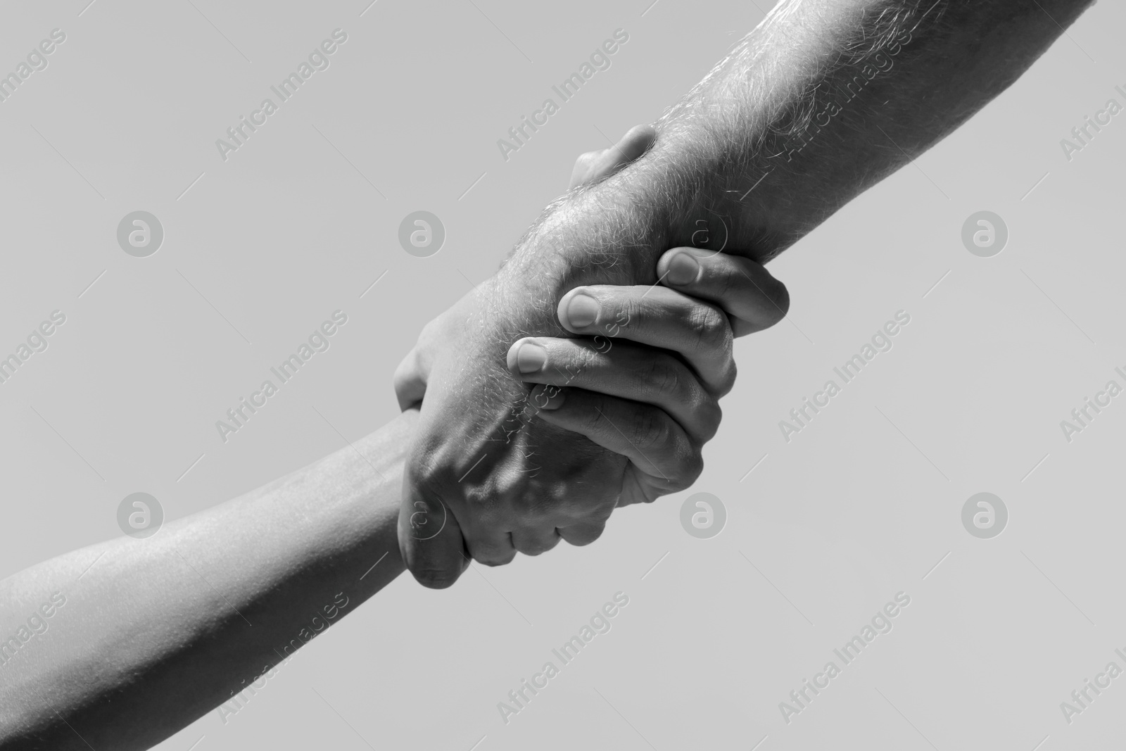 Image of Help and support. People holding hands on light grey background, closeup. Toned in black and white