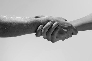 Image of Help and support. People holding hands on light grey background, closeup. Toned in black and white