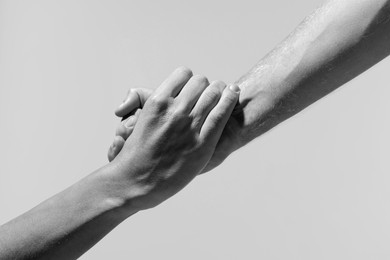 Image of Help and support. People holding hands on light grey background, closeup. Toned in black and white