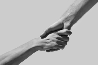 Image of Help and support. People holding hands on light grey background, closeup. Toned in black and white