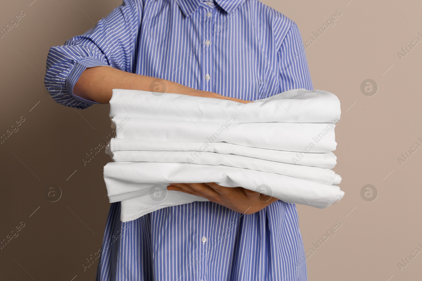 Photo of Woman holding stack of clean bed linens on beige background