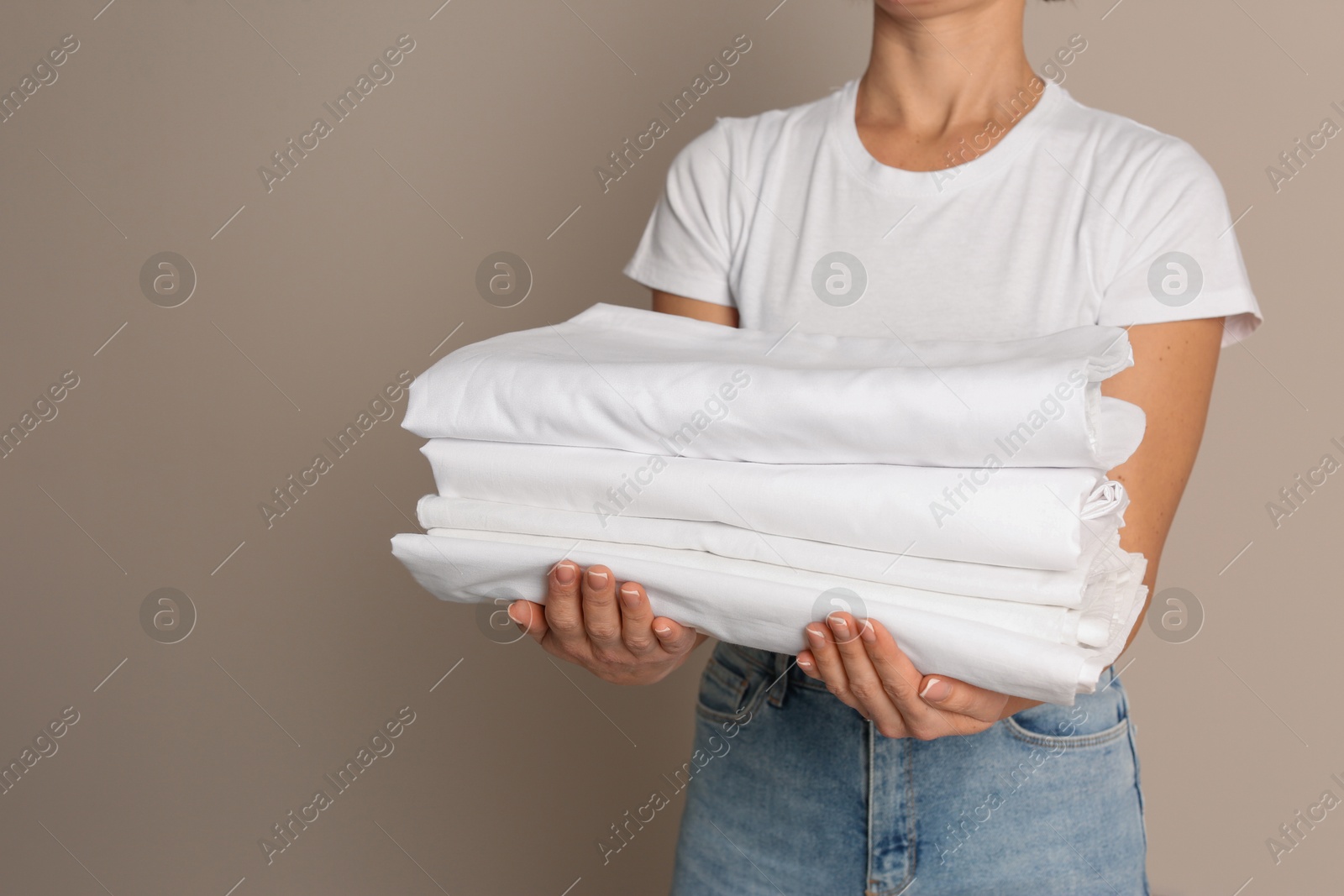 Photo of Woman holding stack of clean bed linens on beige background