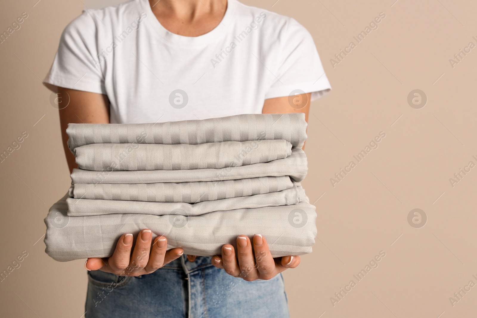 Photo of Woman holding stack of clean bed linens on beige background