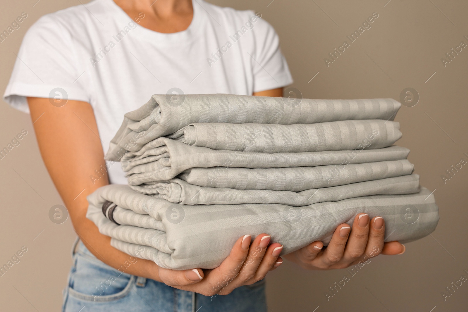 Photo of Woman holding stack of clean bed linens on beige background