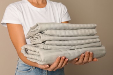 Photo of Woman holding stack of clean bed linens on beige background