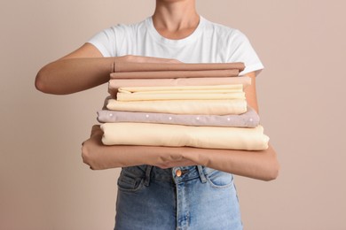 Photo of Woman holding stack of clean bed linens on beige background