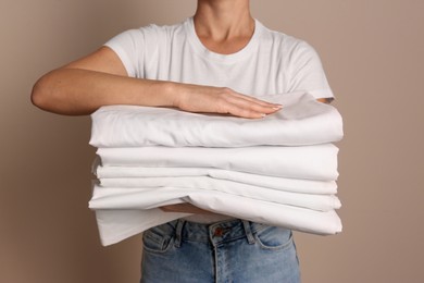 Photo of Woman holding stack of clean bed linens on beige background