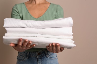 Photo of Woman holding stack of clean bed linens on beige background