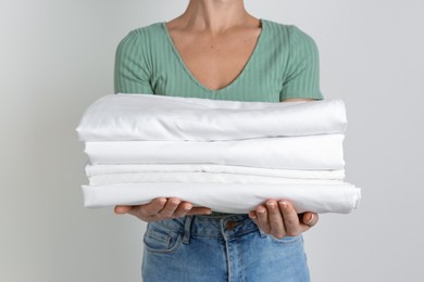 Photo of Woman holding stack of clean bed linens on light grey background