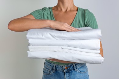 Woman holding stack of clean bed linens on light grey background