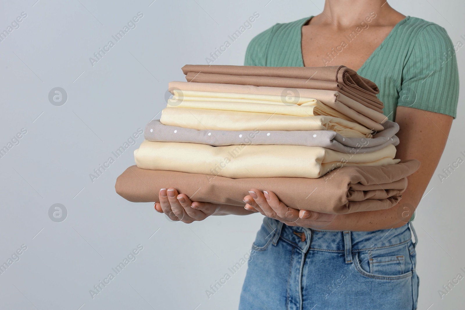 Photo of Woman holding stack of clean bed linens on light grey background. Space for text