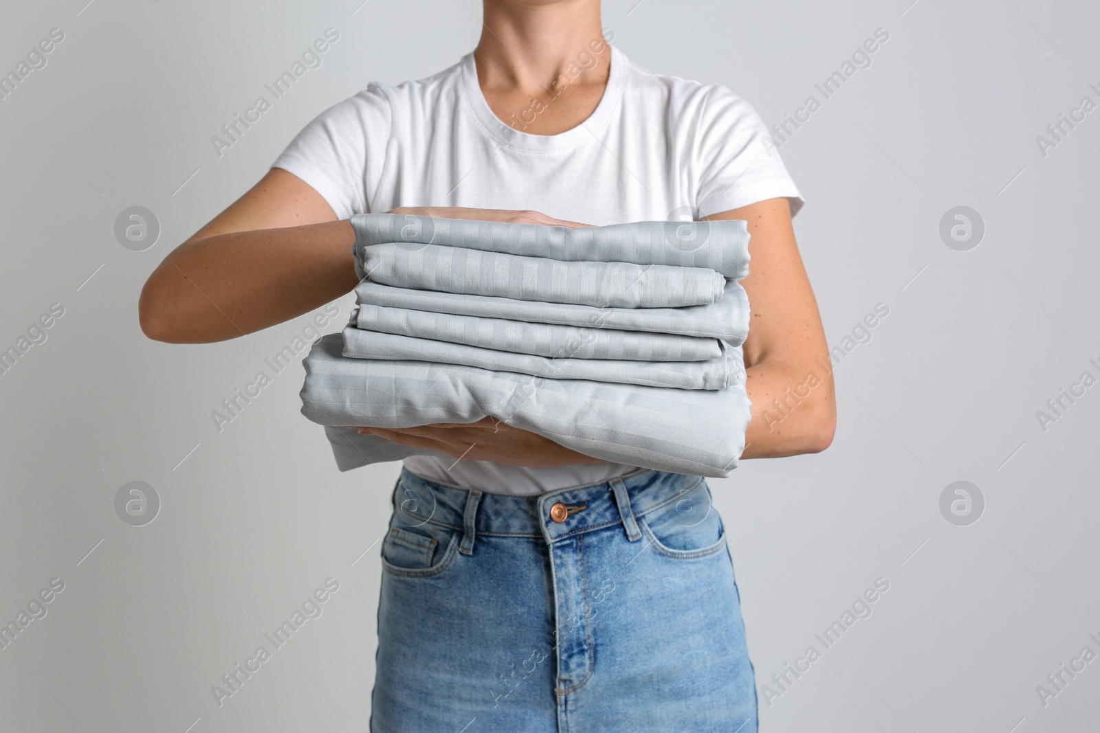 Photo of Woman holding stack of clean bed linens on light grey background