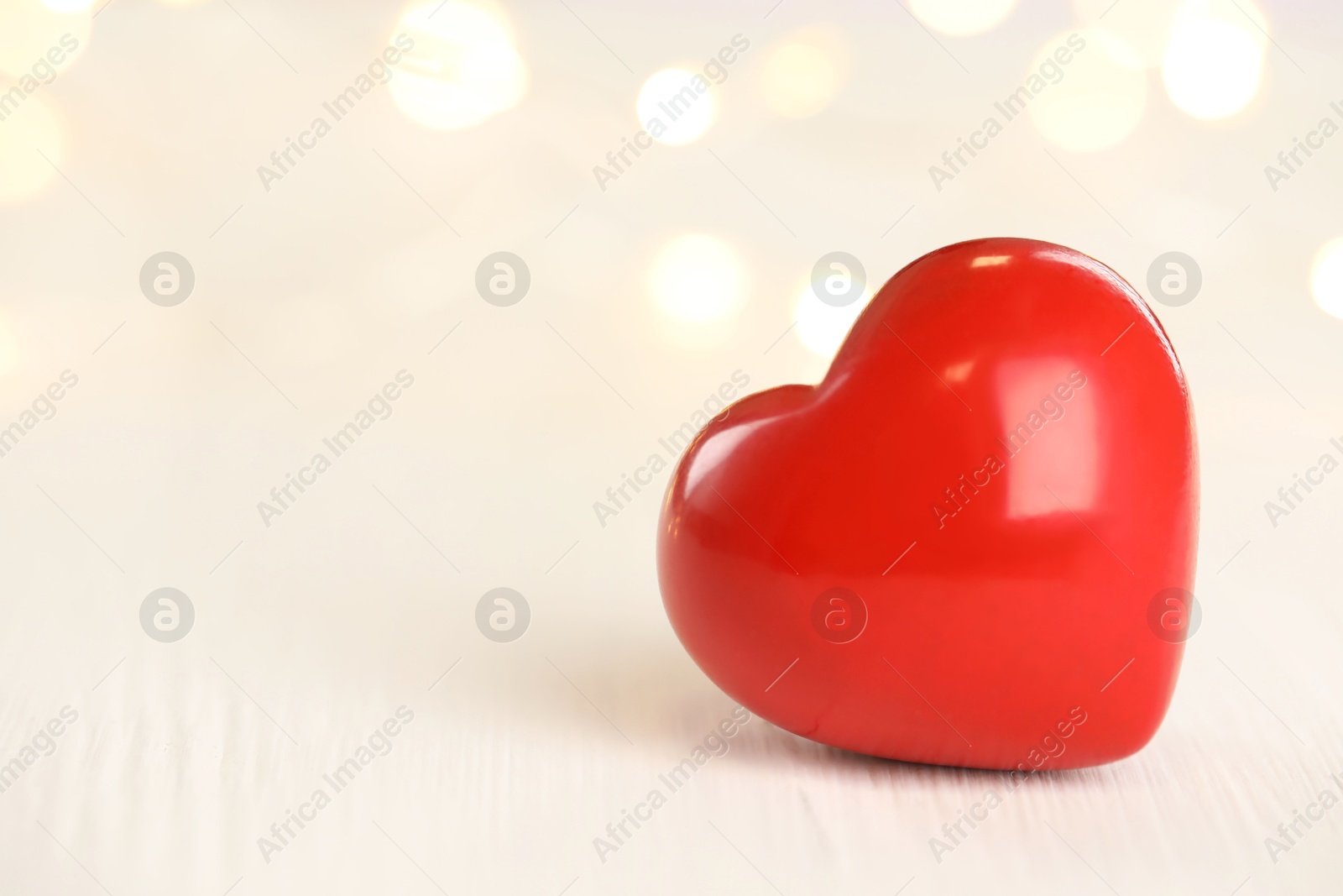 Photo of Red heart on white wooden table against festive lights, space for text. St. Valentine's day