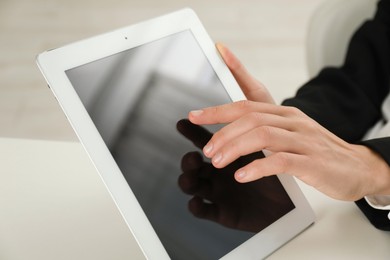 Photo of Businesswoman using tablet at white table indoors, closeup. Modern technology