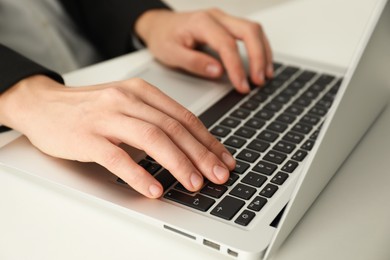 Photo of Businesswoman using laptop at white table indoors, closeup. Modern technology