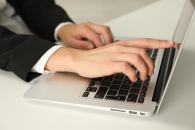 Photo of Businesswoman using laptop at white table indoors, closeup. Modern technology