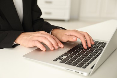 Photo of Businesswoman using laptop at white table indoors, closeup. Modern technology