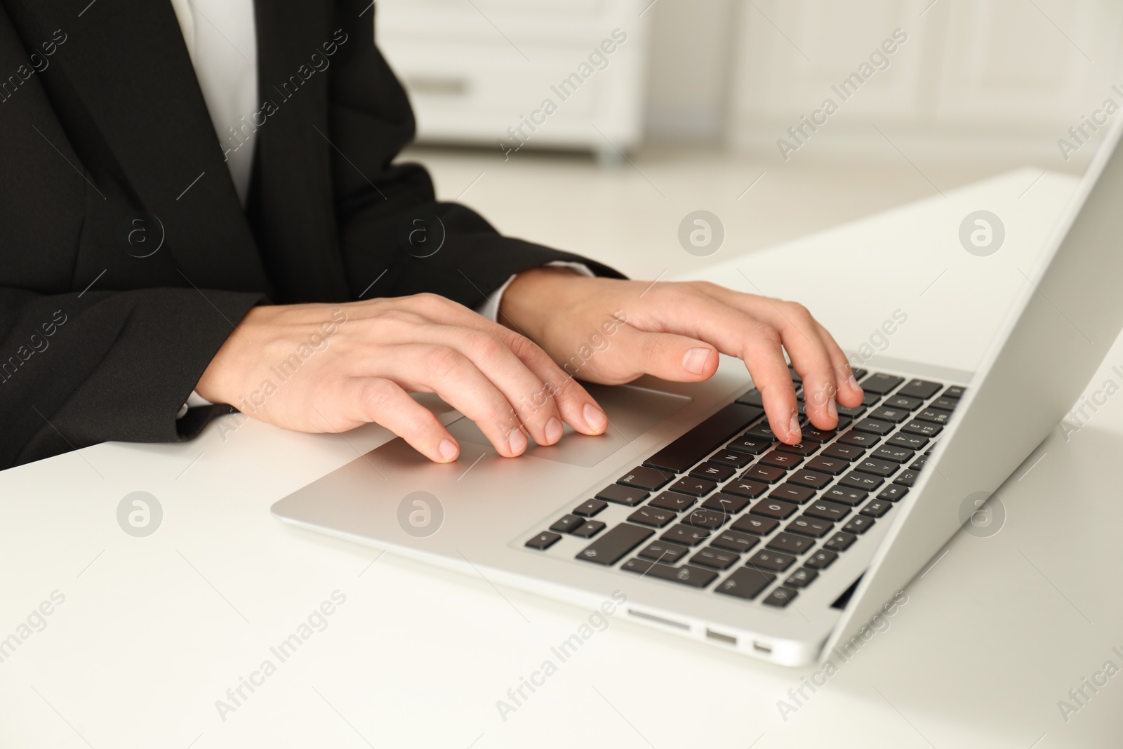 Photo of Businesswoman using laptop at white table indoors, closeup. Modern technology