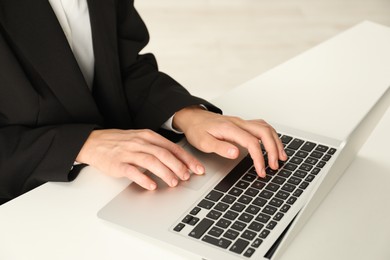 Photo of Businesswoman using laptop at white table indoors, closeup. Modern technology