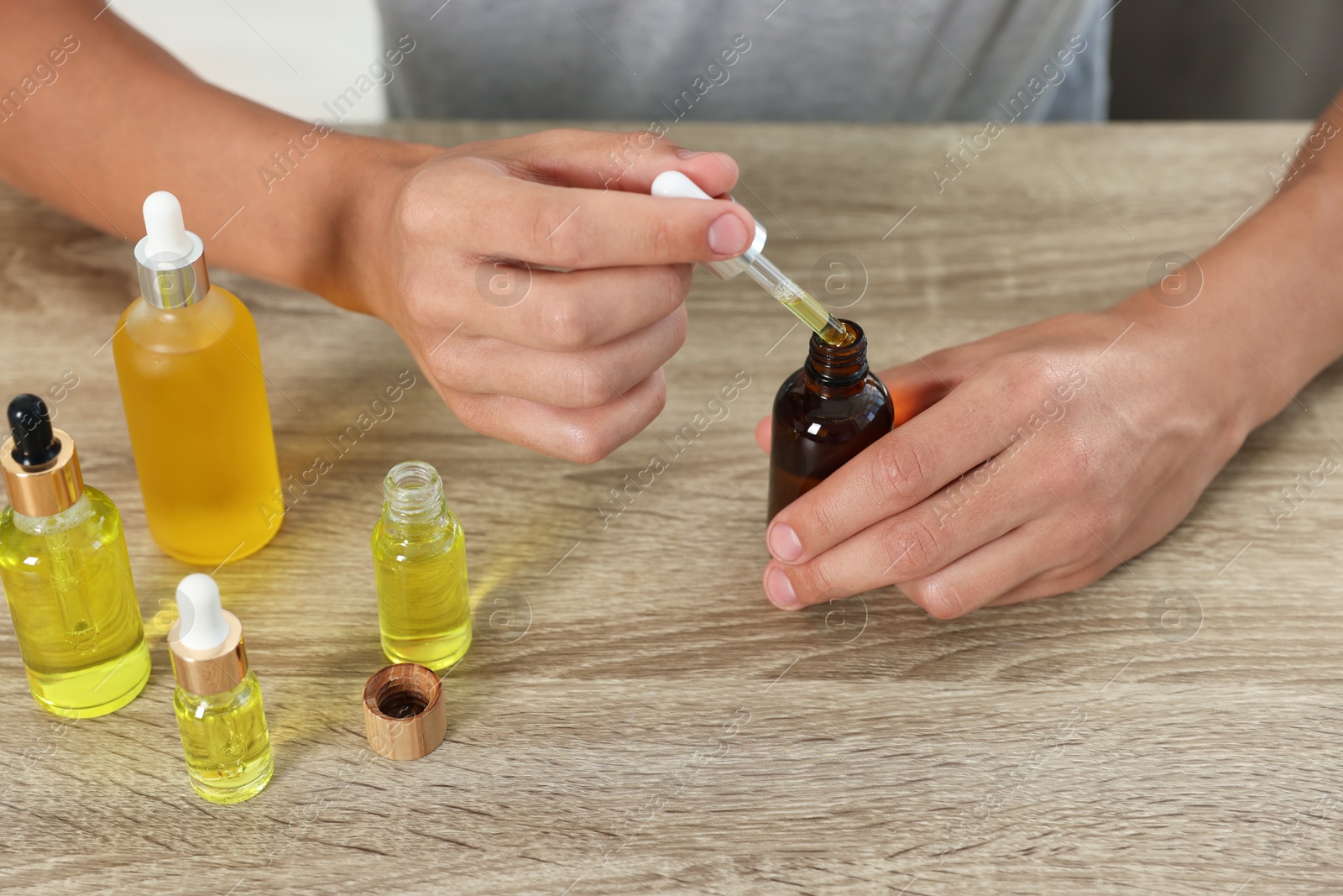 Photo of Young man dripping CBD tincture into bottle from dropper at wooden table, closeup