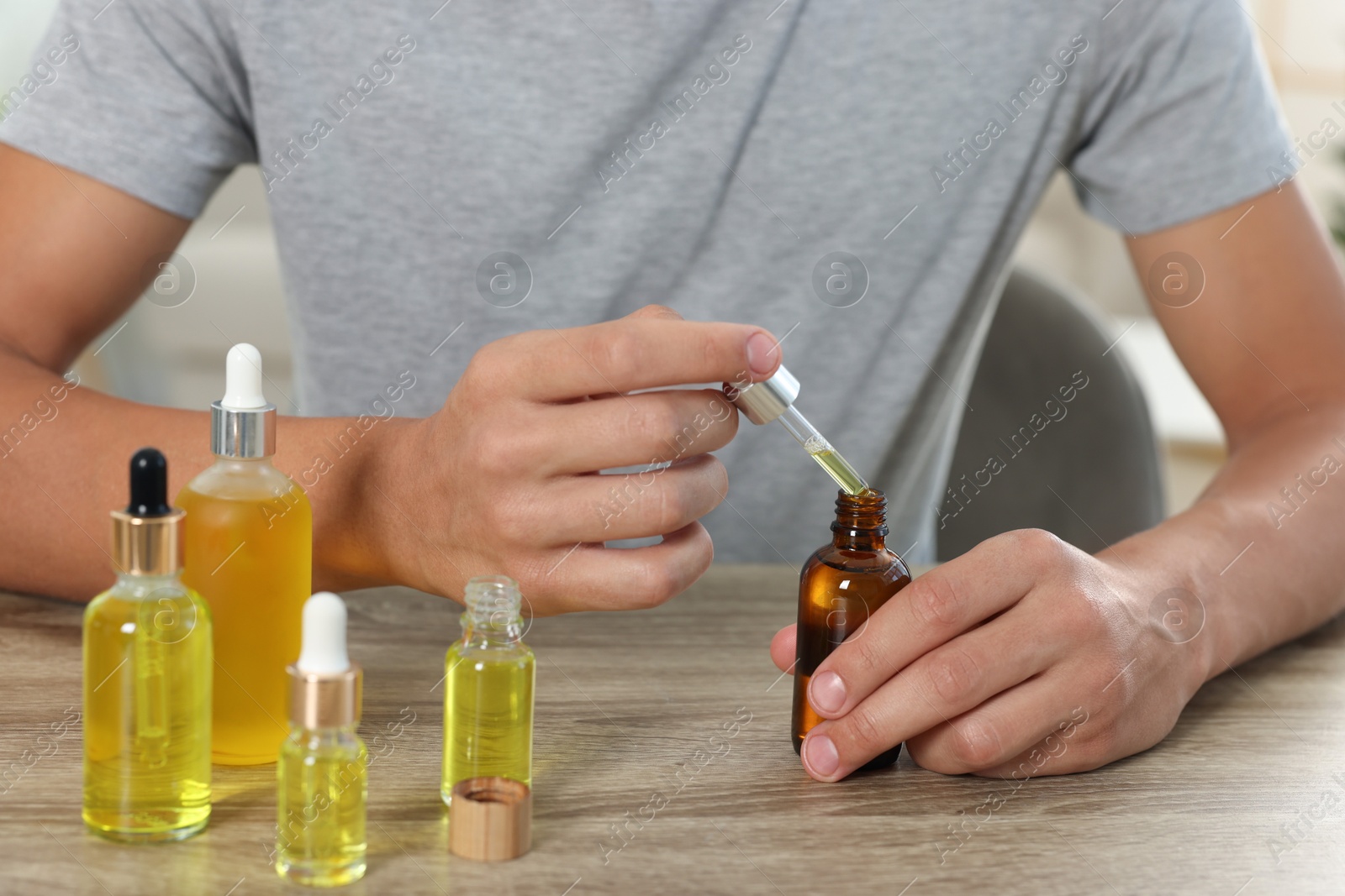 Photo of Young man dripping CBD tincture into bottle from dropper at wooden table, closeup