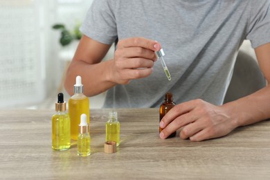 Photo of Young man dripping CBD tincture into bottle from dropper at wooden table, closeup