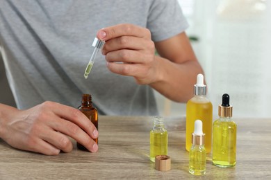 Photo of Young man dripping CBD tincture into bottle from dropper at wooden table, closeup