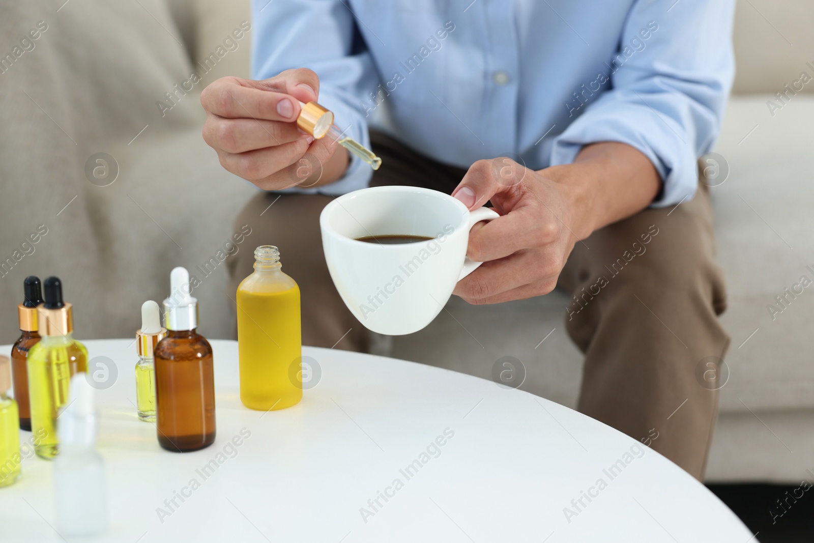 Photo of Young man dripping CBD tincture into drink at white table, closeup