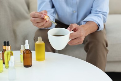 Photo of Young man dripping CBD tincture into drink at white table, closeup