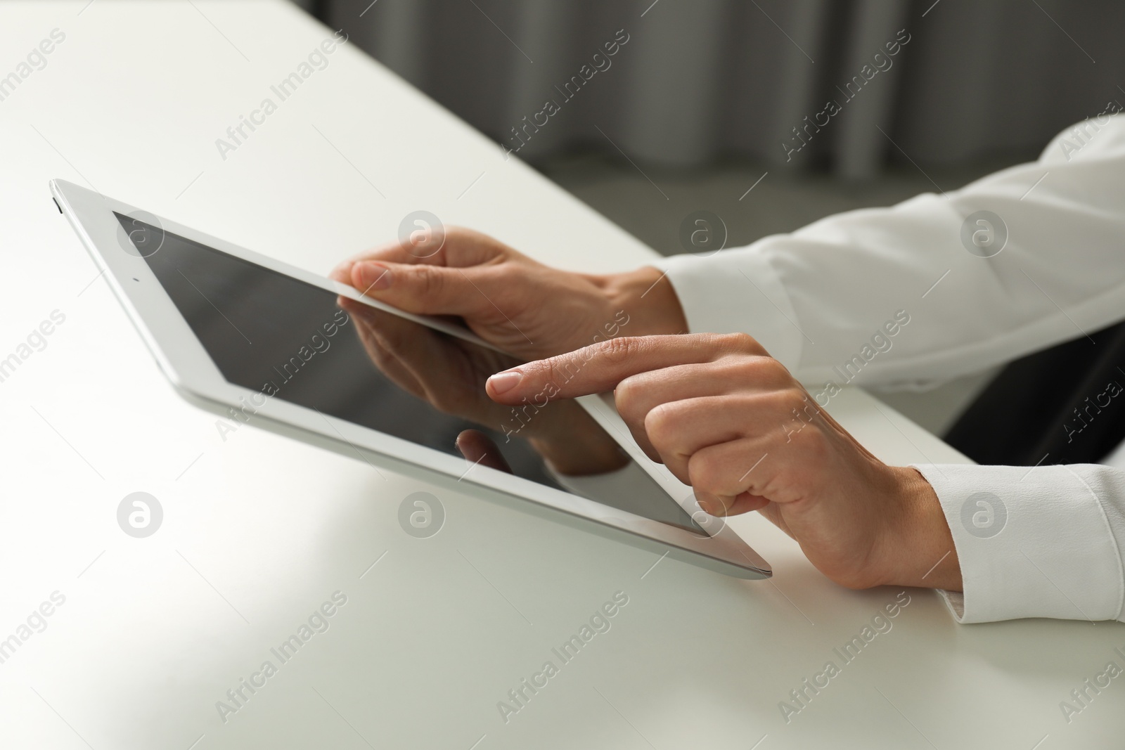 Photo of Businesswoman using tablet at white table indoors, closeup. Modern technology