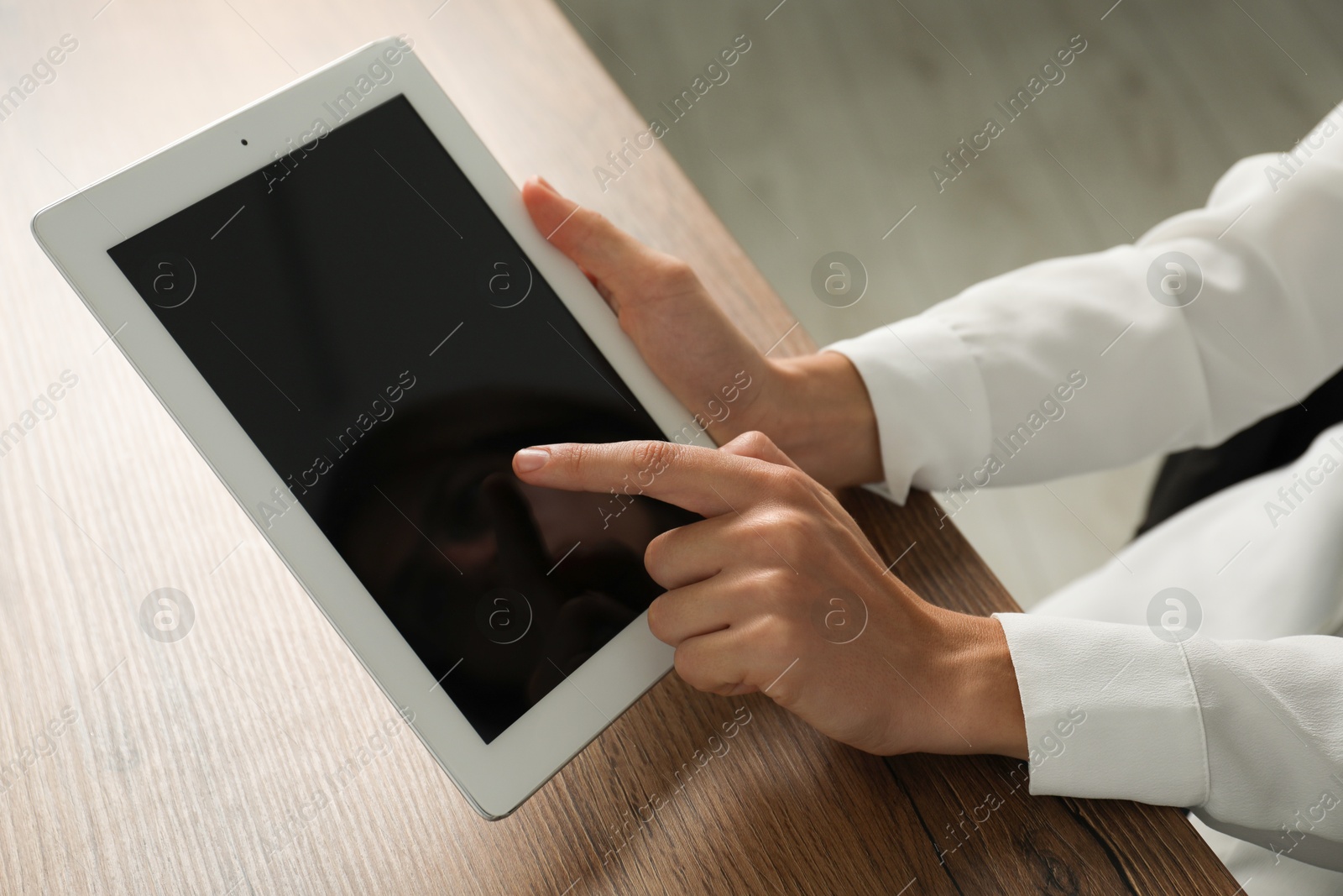 Photo of Businesswoman using tablet at wooden table indoors, closeup. Modern technology