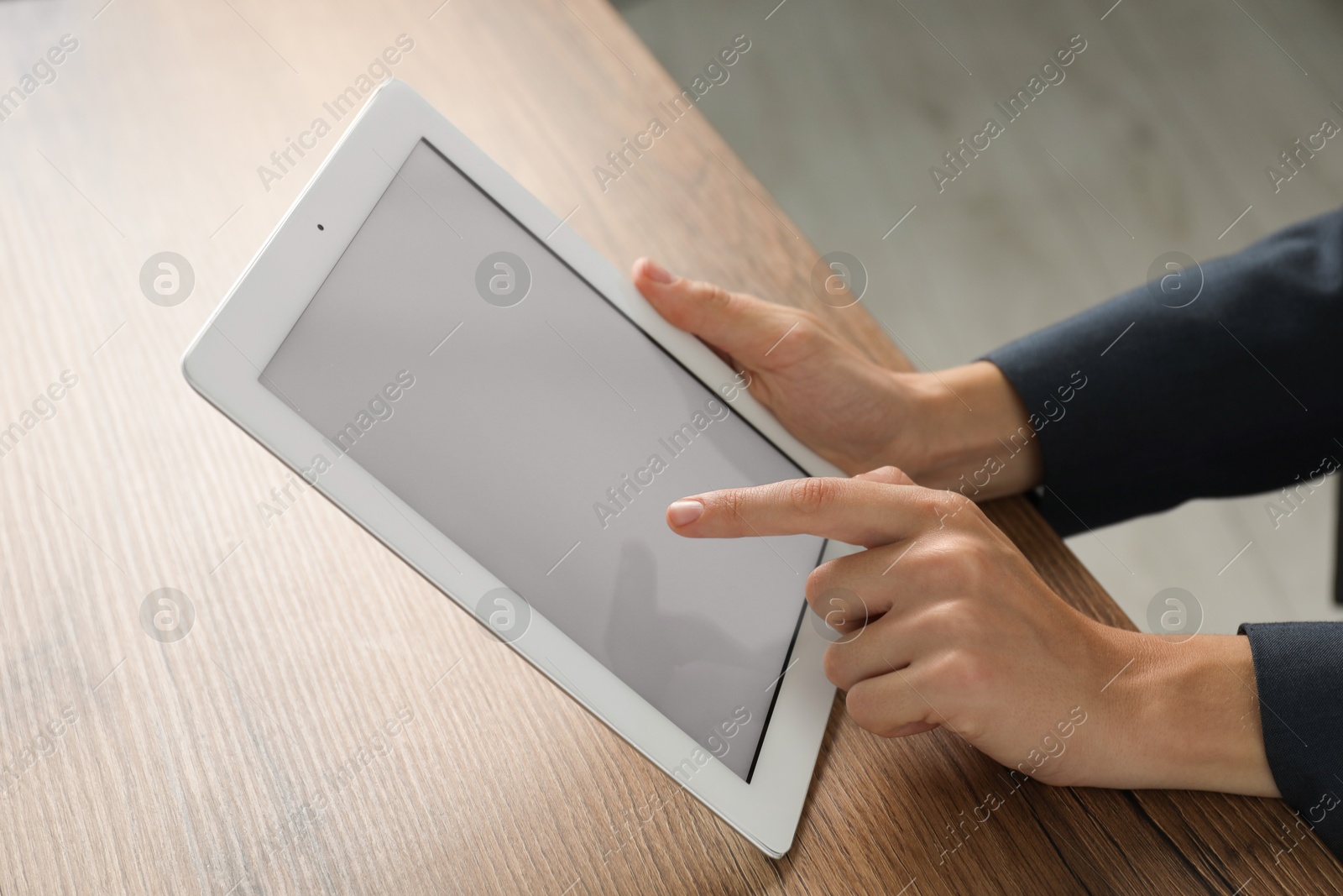 Photo of Businesswoman using tablet at wooden table indoors, closeup. Modern technology